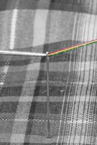 A black and white image of needle and thread but one side of thread is in color.